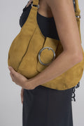 Ruby bag in ochre suede tucked under the arm, close view of the round silver buckle