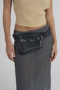 Loulou belt bag in black leather, close view of the snap flap pocket over a grey sheer skirt